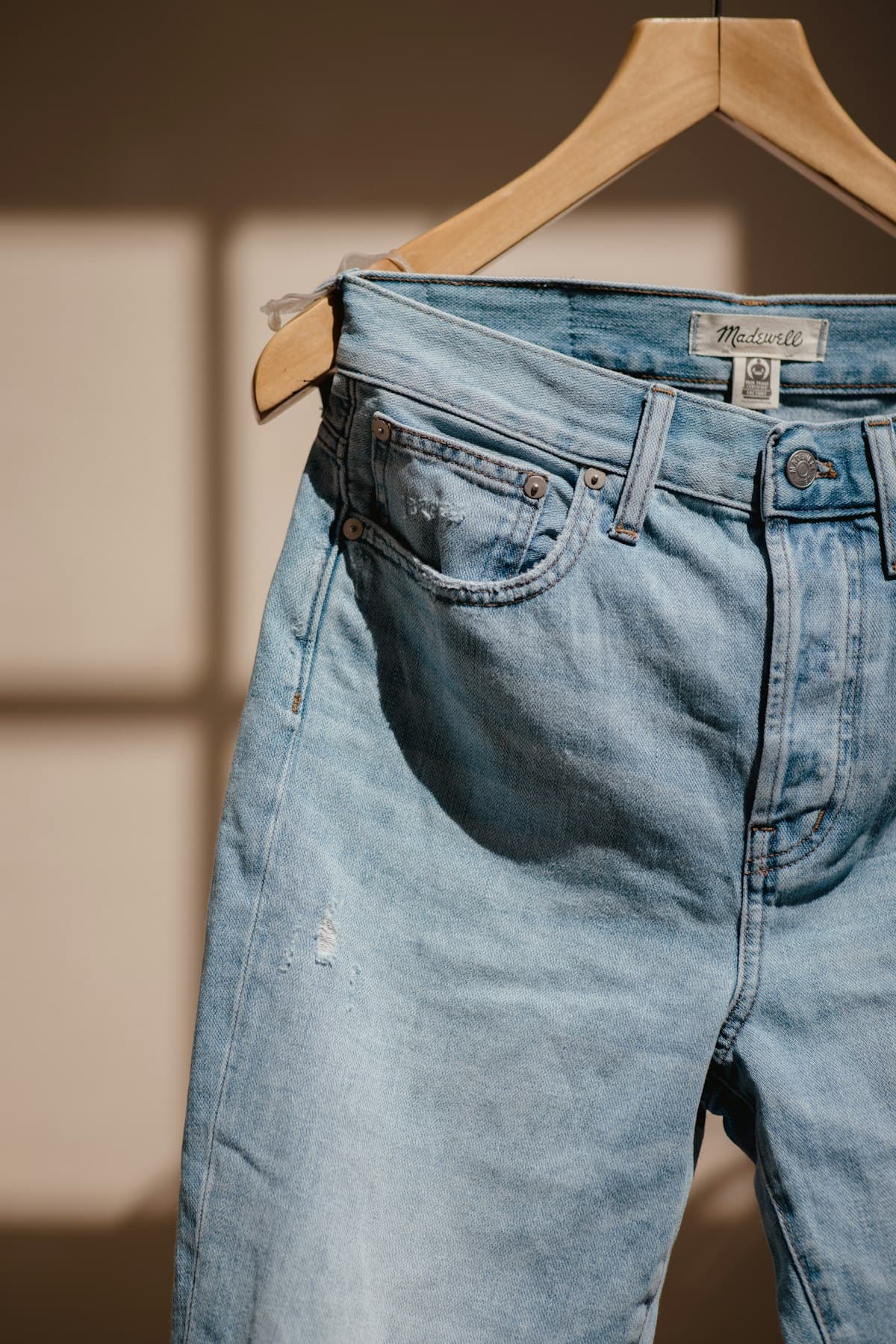 Calça jeans clara pendurada em cabide de madeira